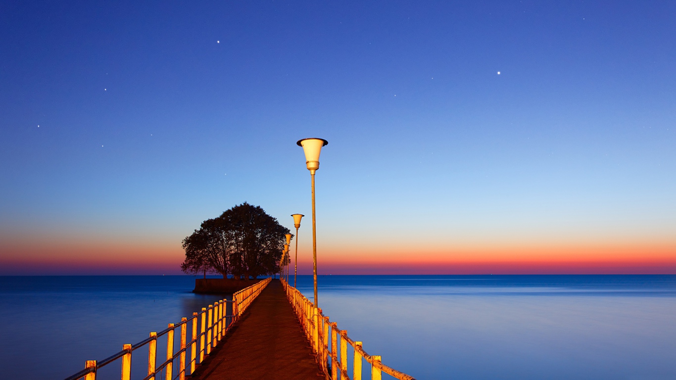 Мост в фонарями в море на закате 