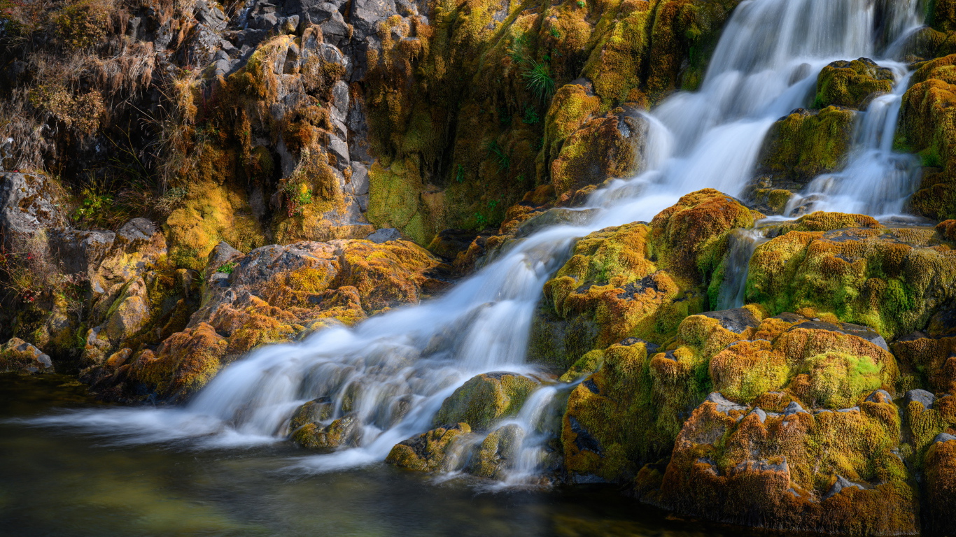 Быстрая вода водопада стекает по покрытым мхом камням, Исландия 