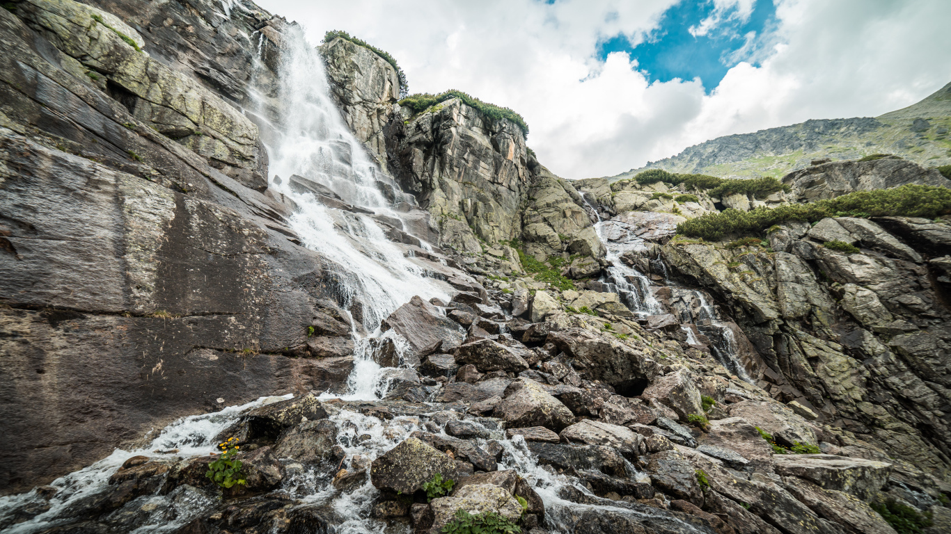 Водопад стекает по камням на фоне неба с белыми облаками