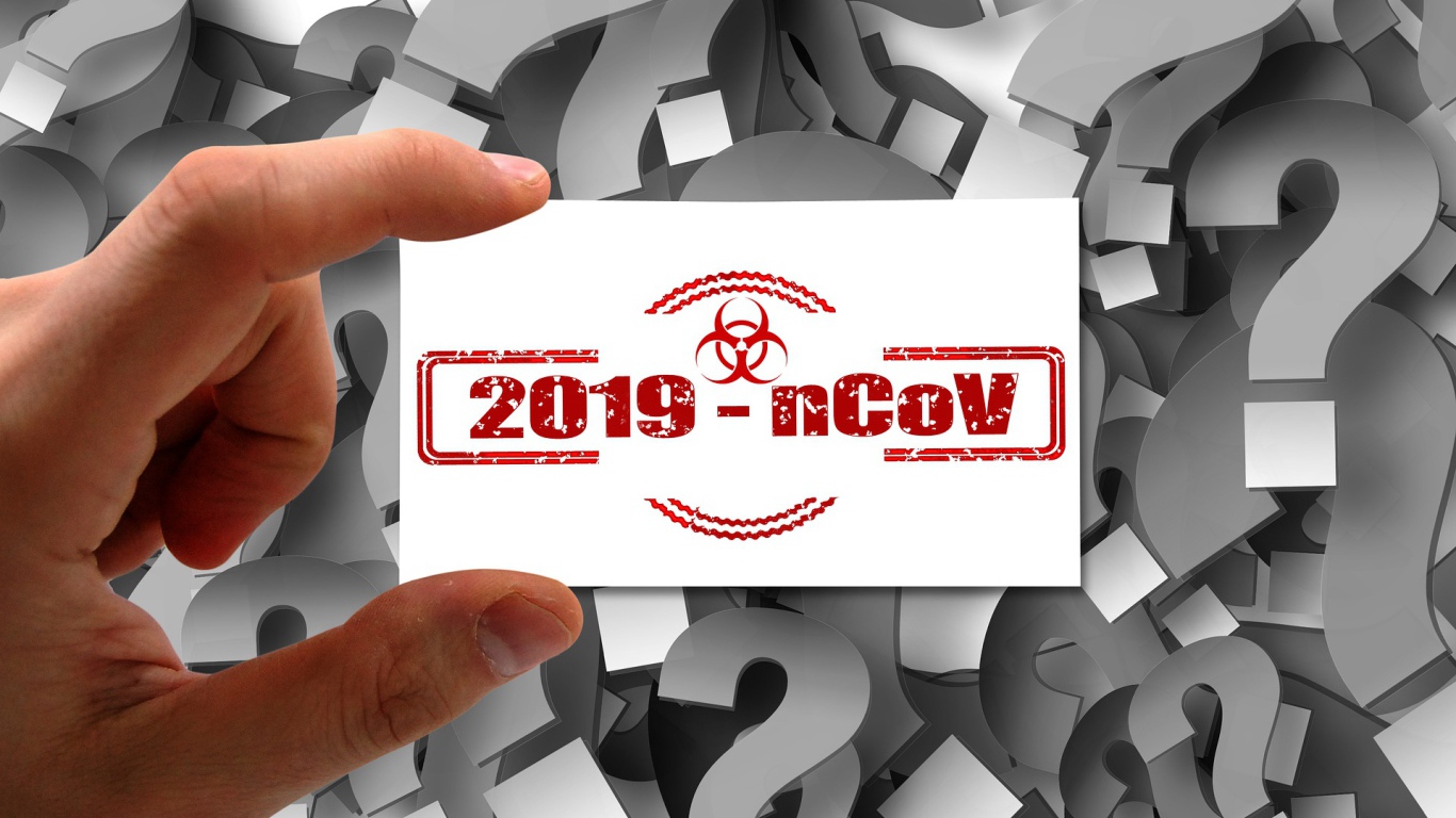 Табличка коронавирус covid-19 в руке на фоне знаков вопроса