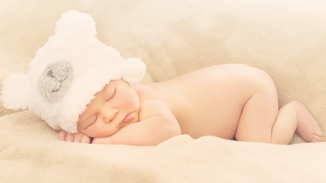 Грудной ребенок с белой шапке спит на кровати