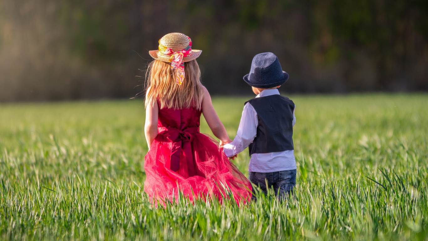 Маленькие мальчик и девочка идут по зеленому полю