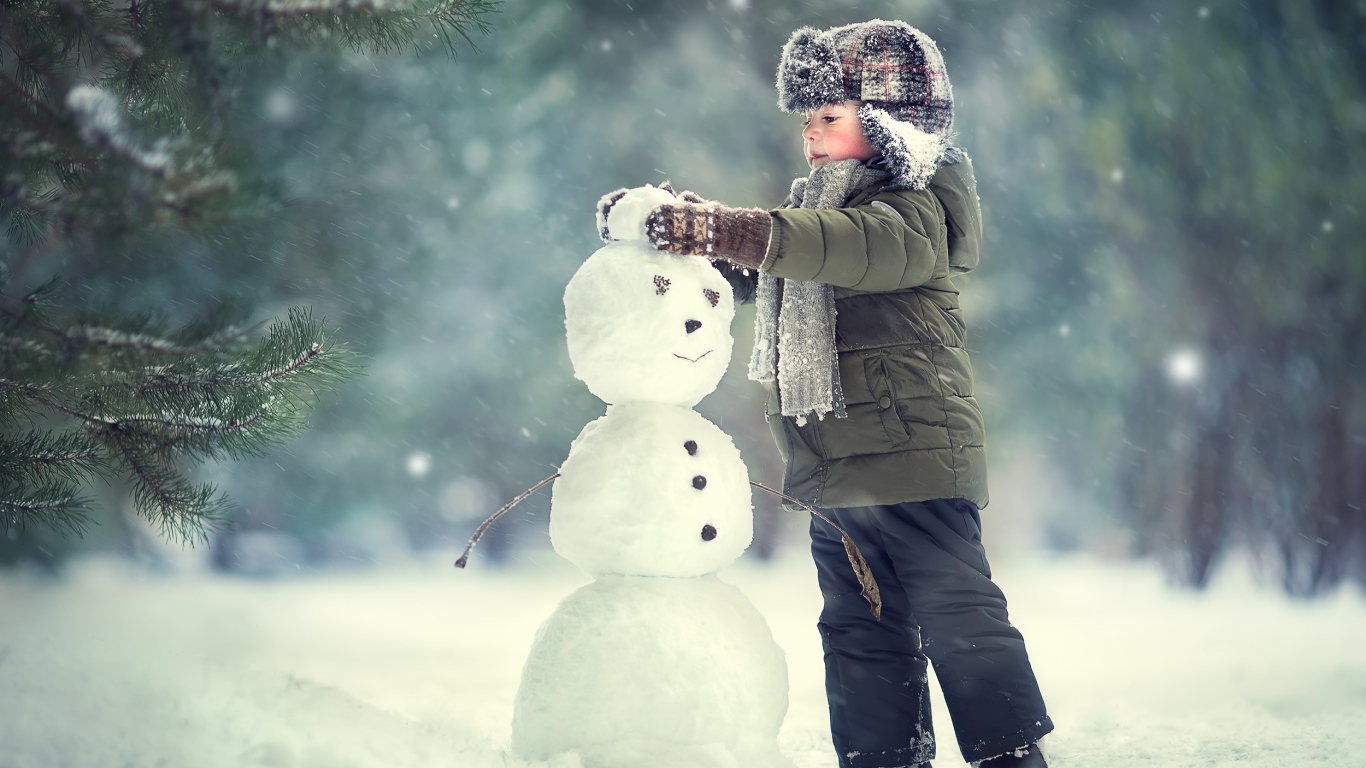 Маленький мальчик лепит снеговика зимой