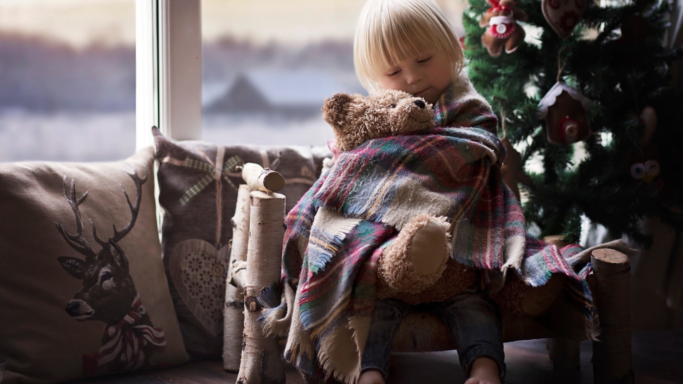 Маленькая девочка обнимает мишку у ели