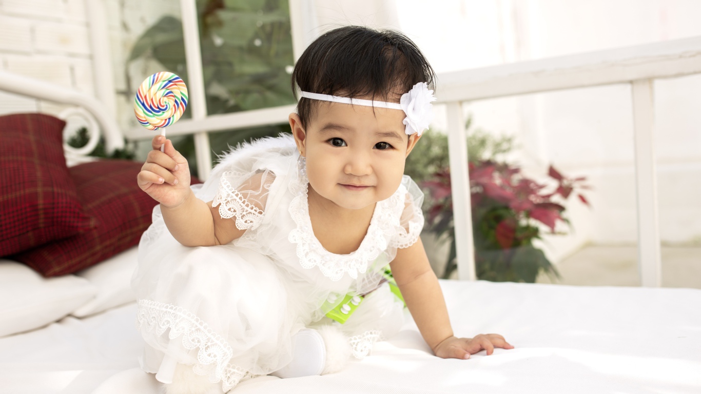 Маленькая девочка в белом платье с леденцом в руке