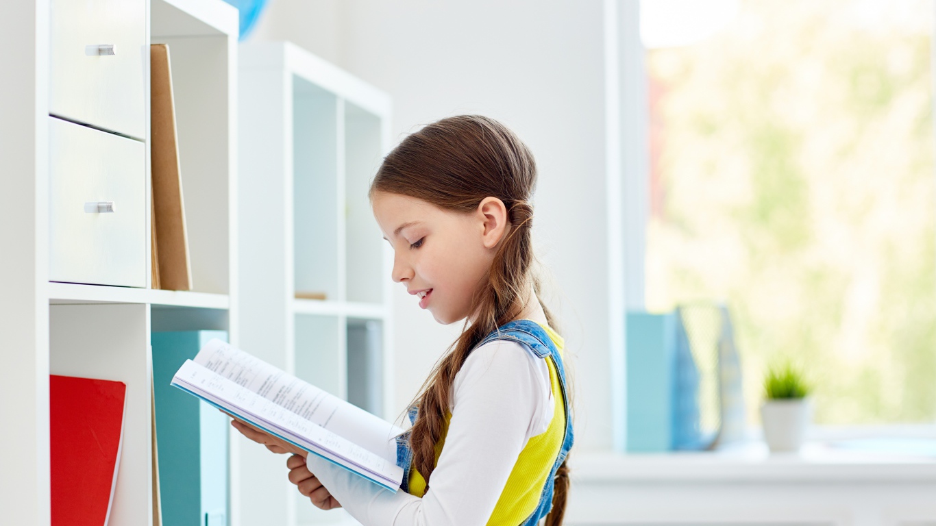 Умная девочка школьница с книгой в библиотеке 