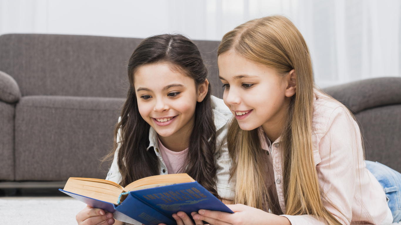 Две маленькие девочки читают книгу на полу