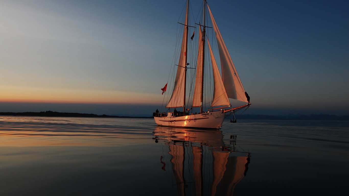 Большая яхта с белыми парусами на закате в море