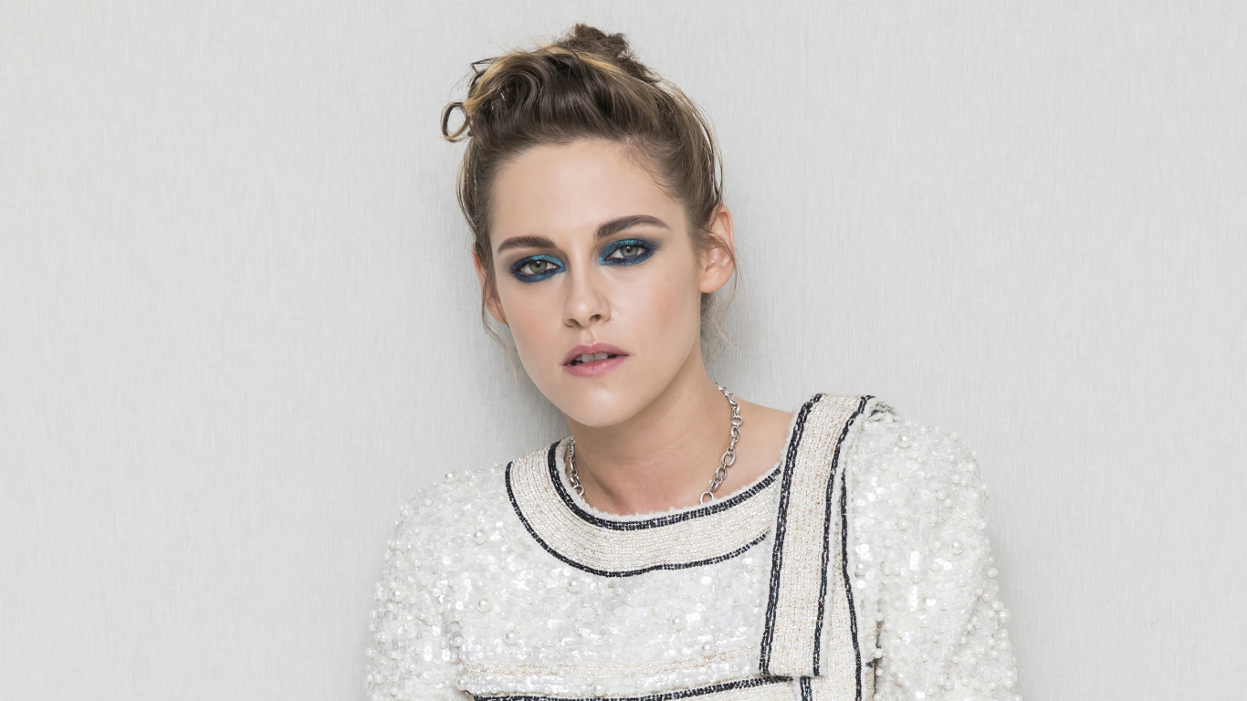 Актриса Кристен Стюарт с накрашенными глазами на фоне серой стены 