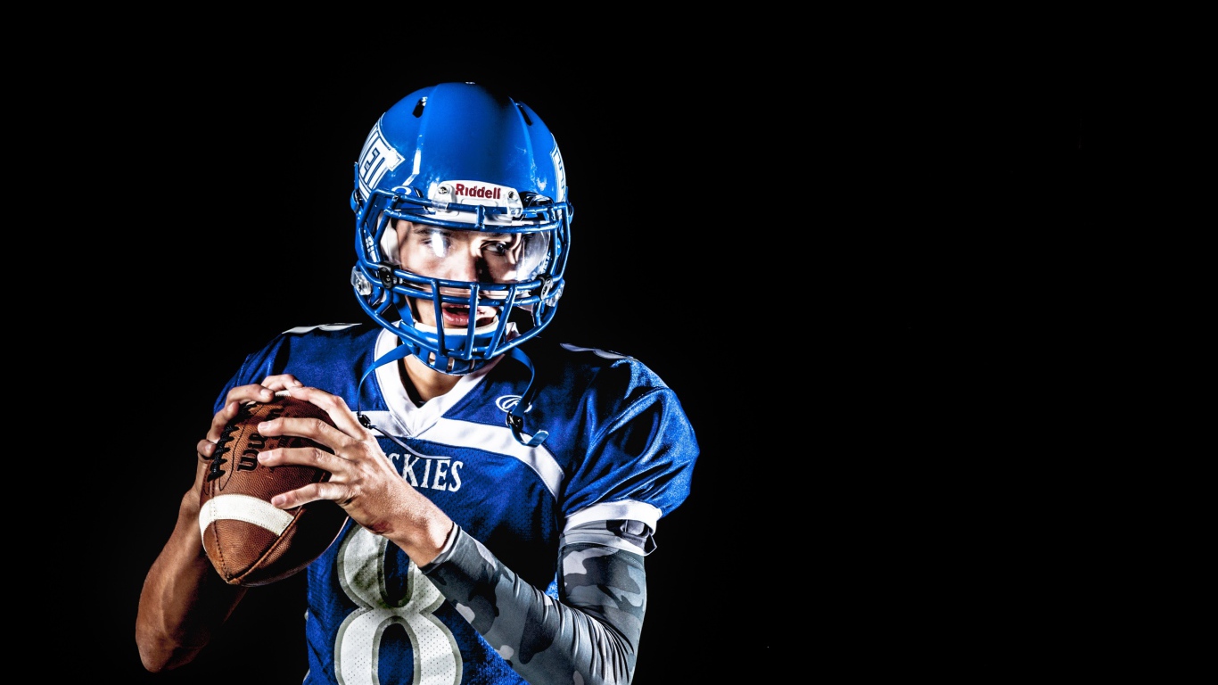 Игрок в американский футбол с мячом в руках на черном фоне 