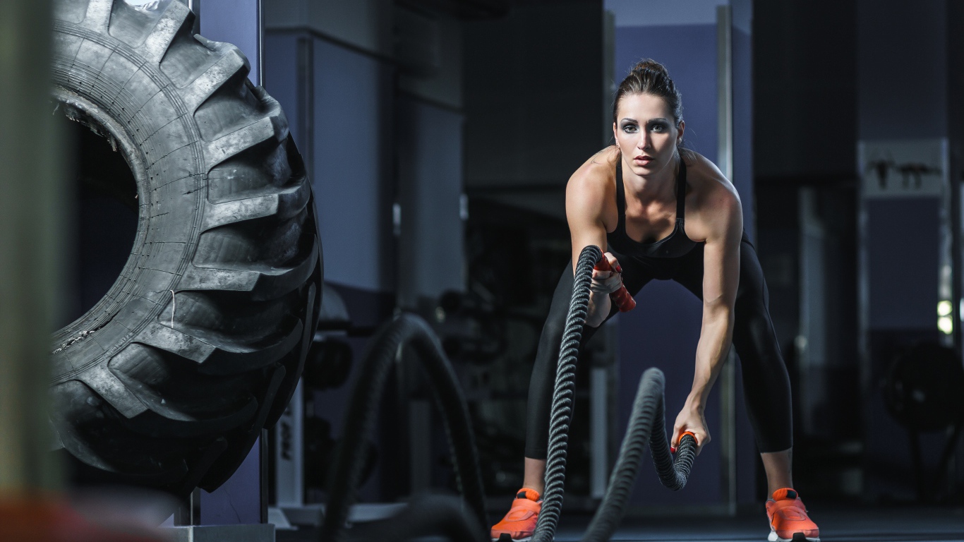 Спортивная девушка занимается с канатами в спортзале 