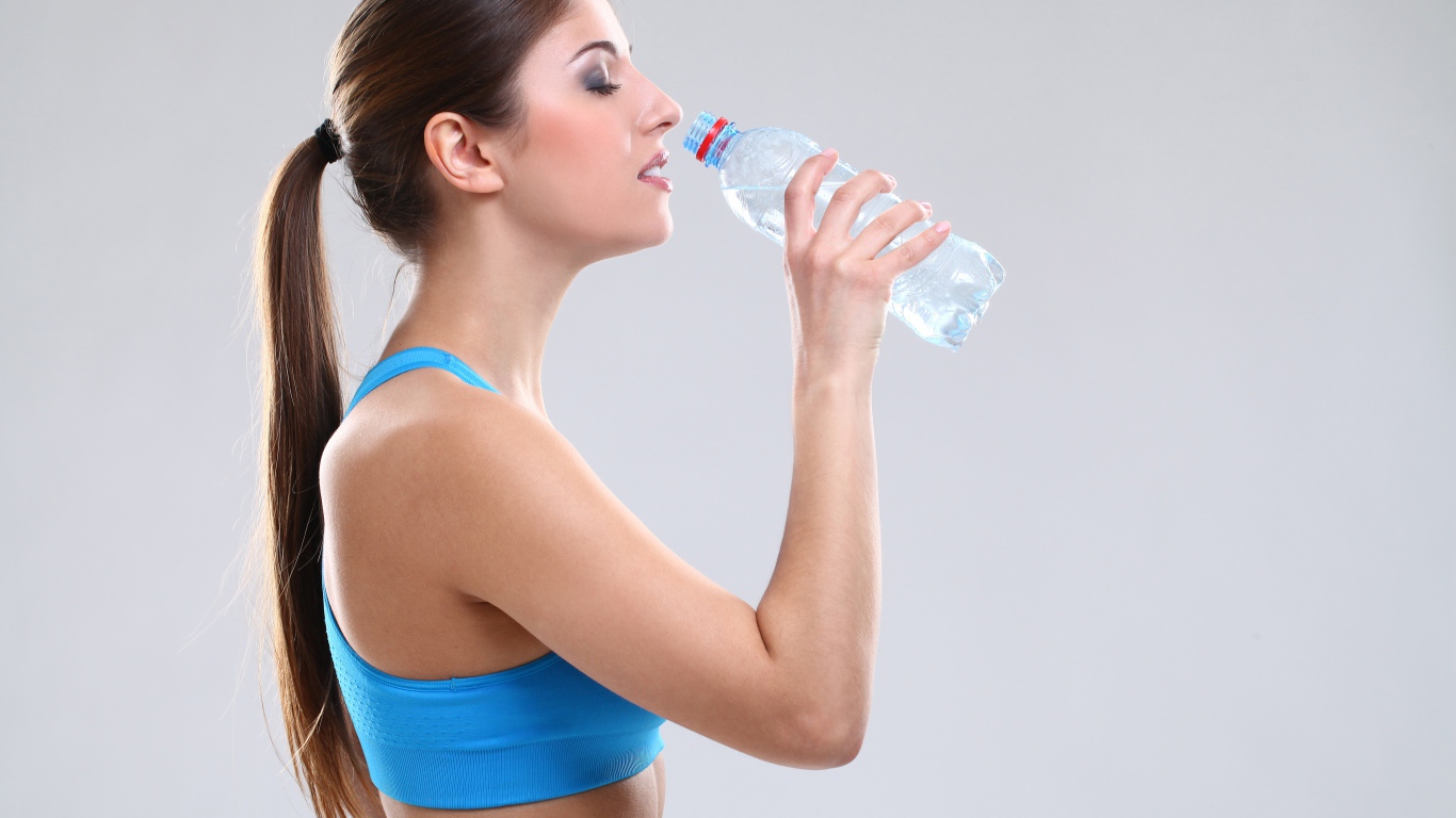 Красивая спортивная девушка пьет воду на сером фоне 