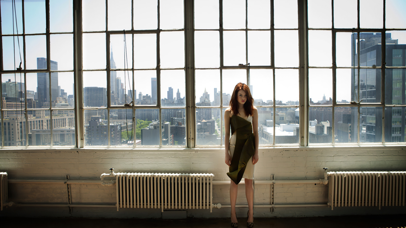 Популярная актриса Эмма Стоун стоит у большого окна