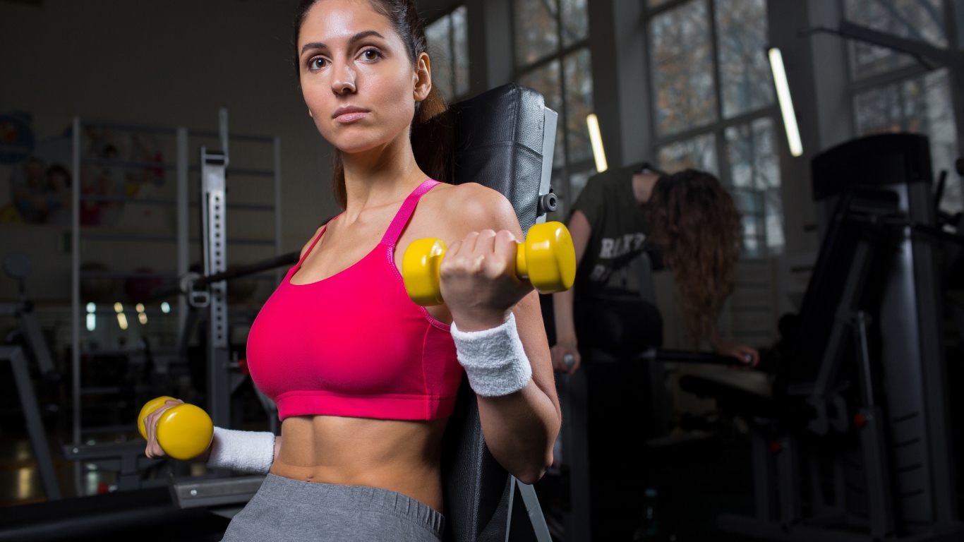 Спортивная девушка качает руки желтыми гантелями в спортзале