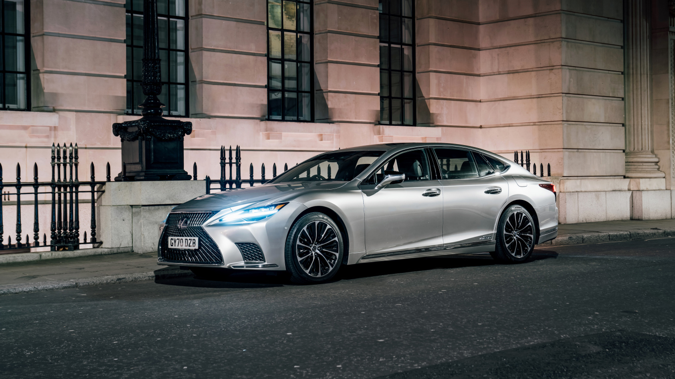 Серебристый автомобиль Lexus LS 500h 2021  года с включенными фарами