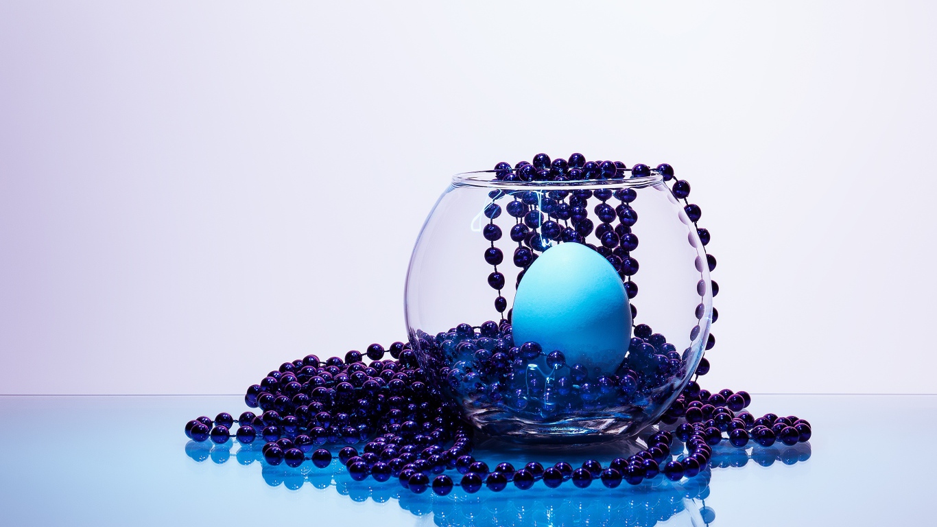 Синие бусы на столе со стеклянной вазой и яйцом