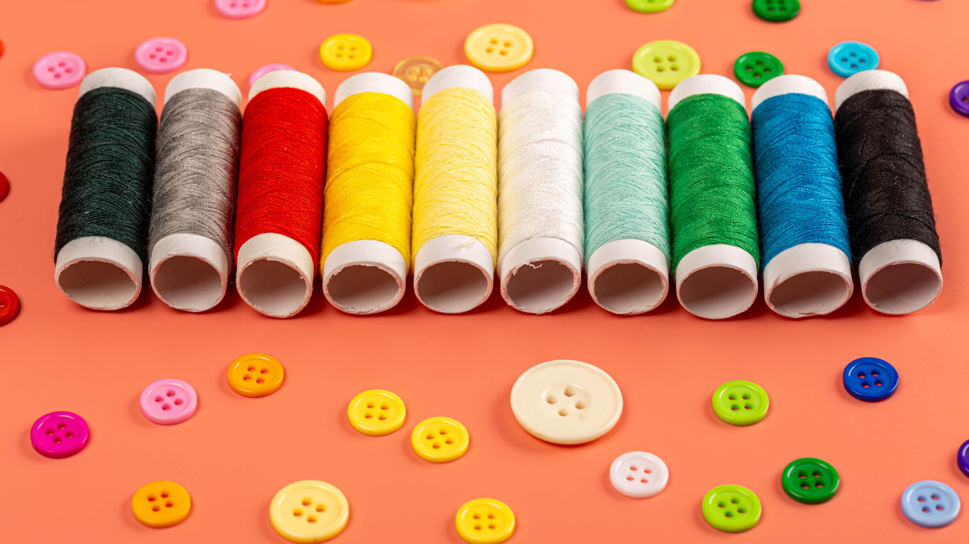 Разноцветные нитки и пуговицы на розовом фоне