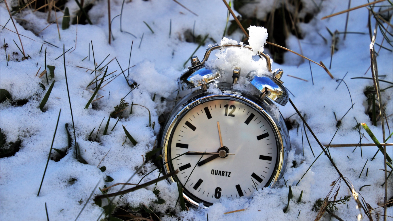 Серебряный будильник лежит в снегу