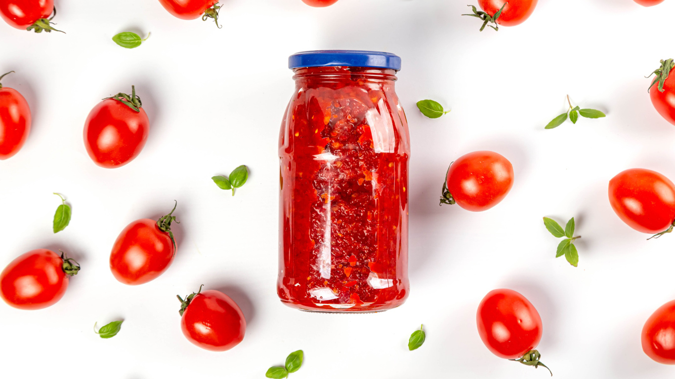 Банка аджики на белом фоне с помидорами