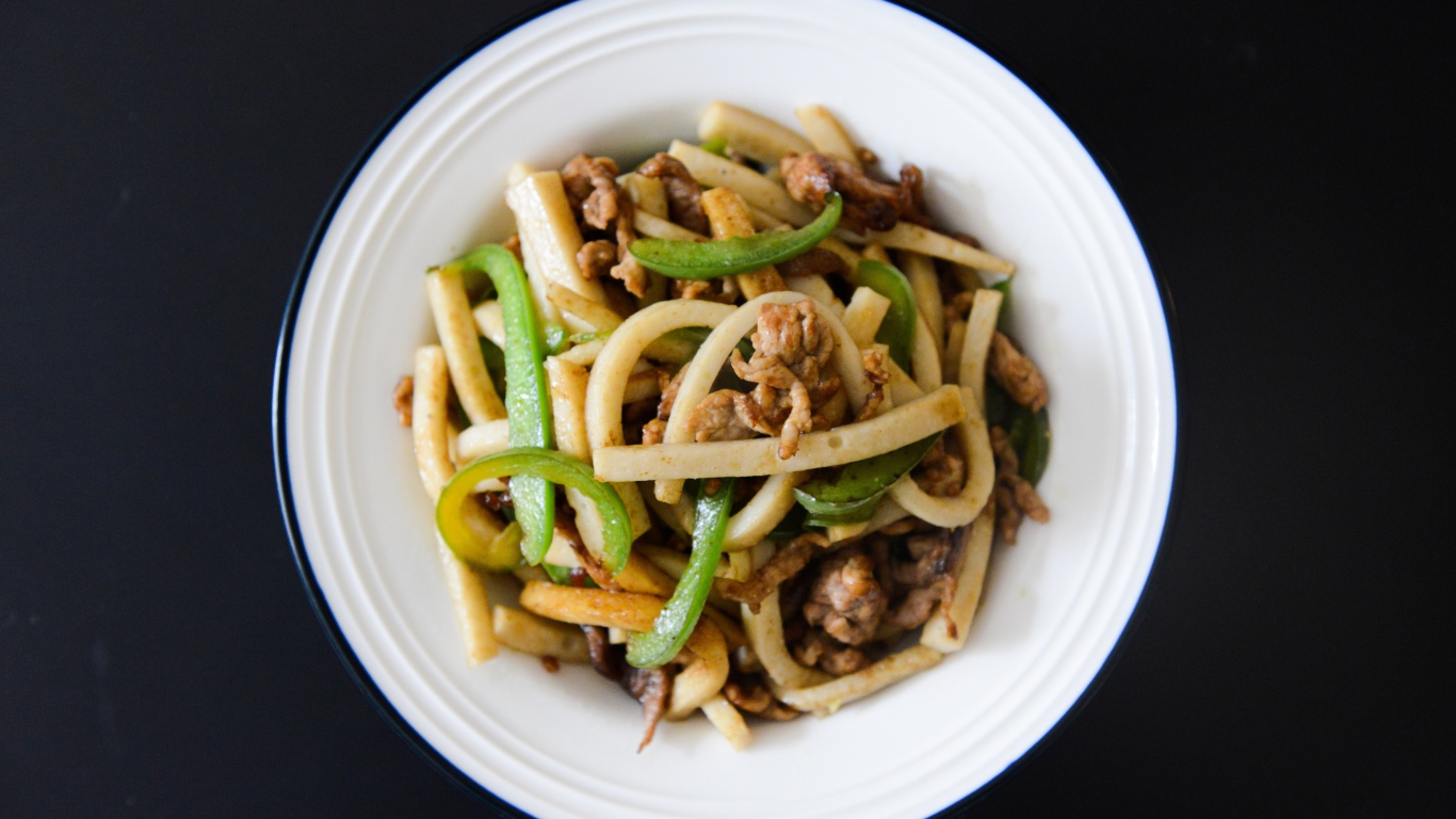 Салат с мясом в белой тарелке на черном фоне