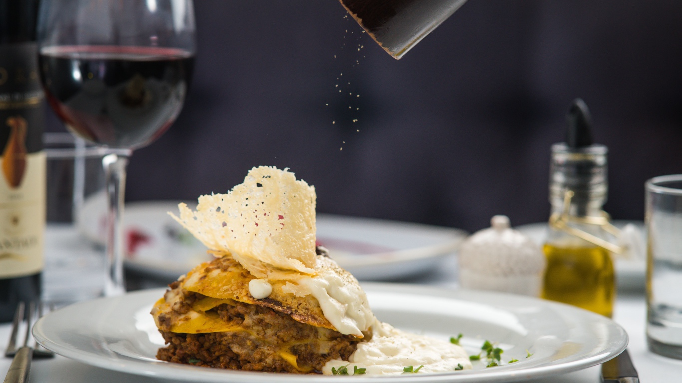 Кусок лазаньи посыпают перцем 