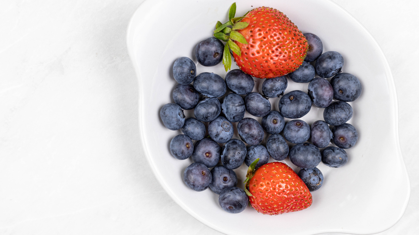 Много синей черники с клубникой в белой тарелке 