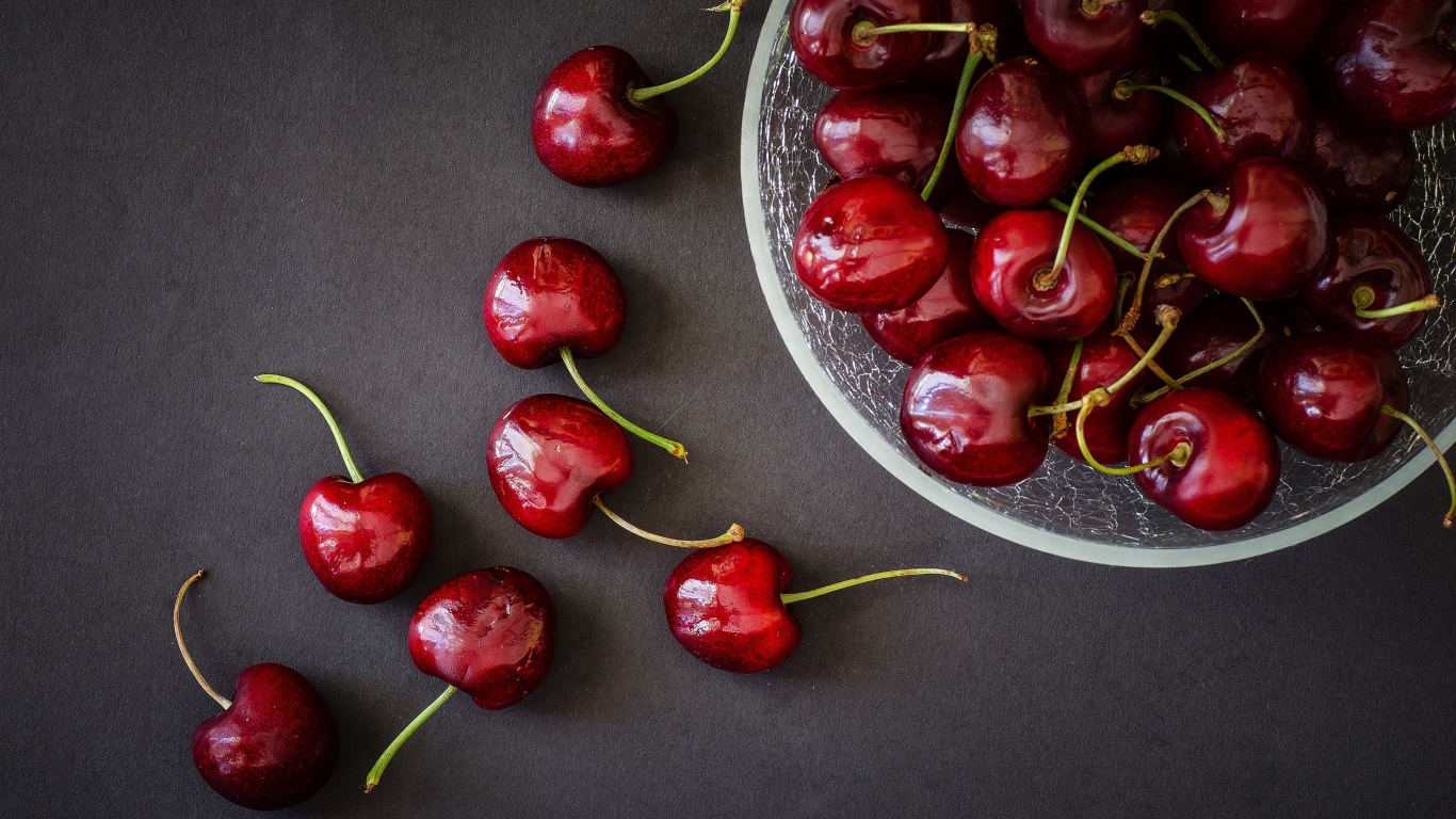 Красные черешни в миске на сером фоне