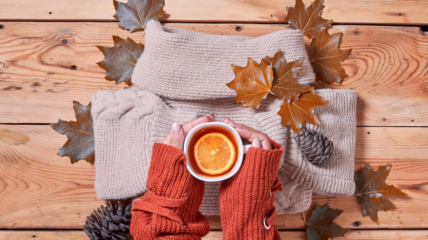 Чашка горячего чая с лимоном в руках на столе с теплым свитером