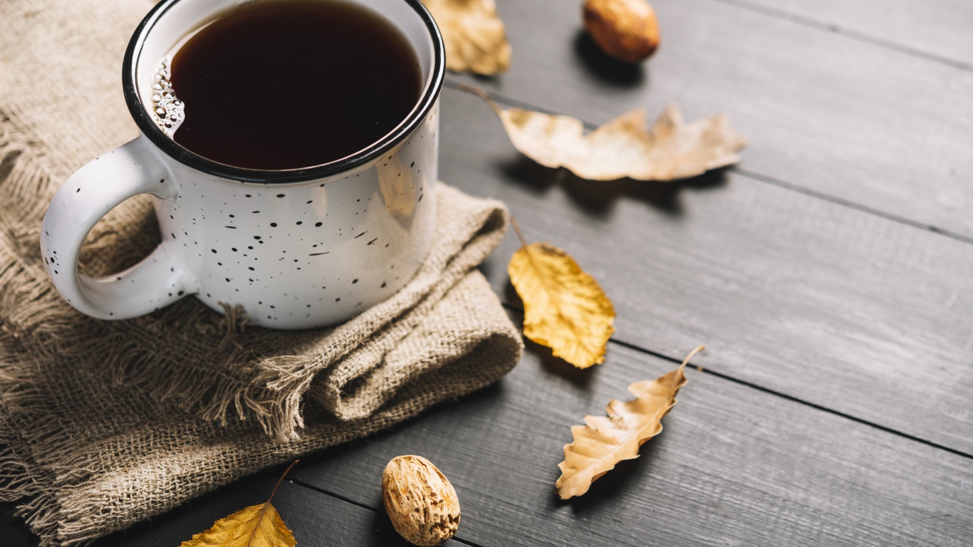 Кружка кофе на столе с листьями и пледом