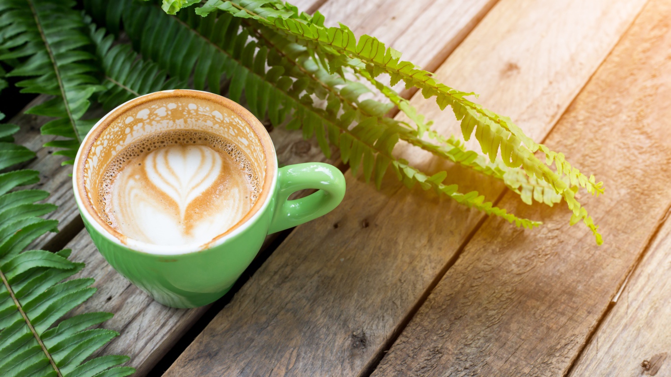 Чашка вкусного капучино  на столе с листьями папоротника