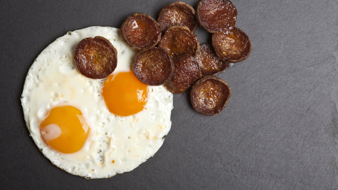 Жареная колбаса с яичницей глазуньей на сером столе 