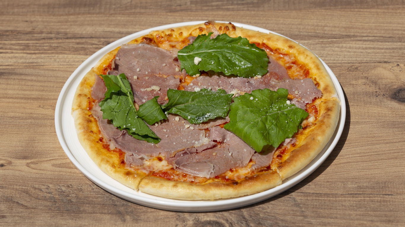 Пицца с кусочками мяса и зеленью на столе