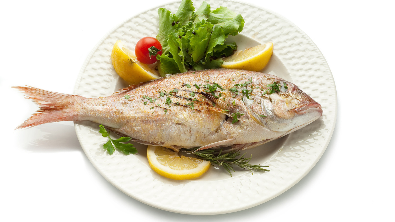 Запеченная рыба на тарелке с зеленью и лимоном