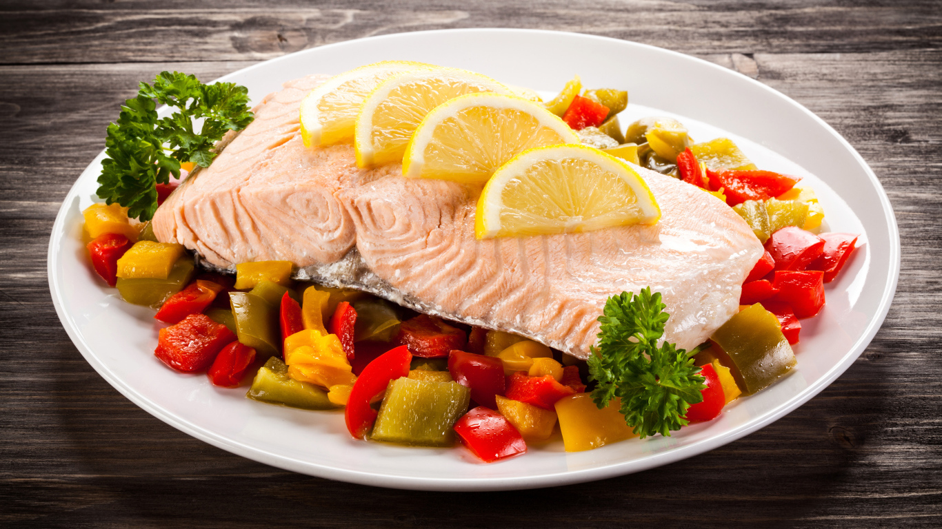Кусок рыбы на тарелке с овощами и лимоном