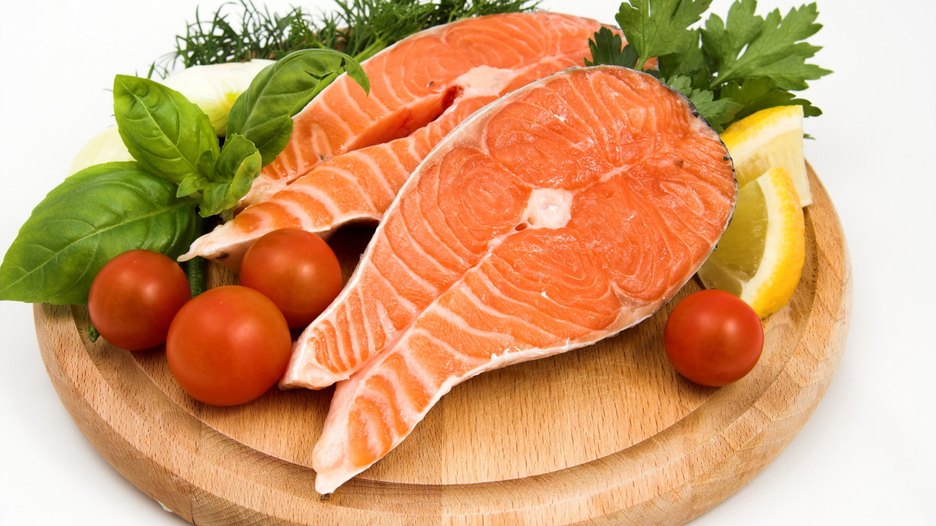 Два куска красной рыбы на доске с зеленью и помидорами