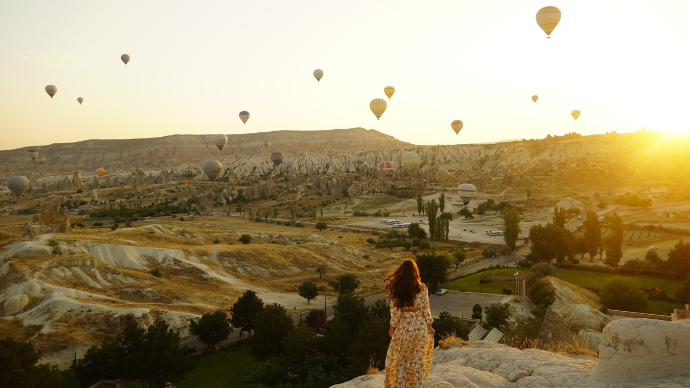 Девушка стоит на краю скалы на фоне неба с воздушными шарами