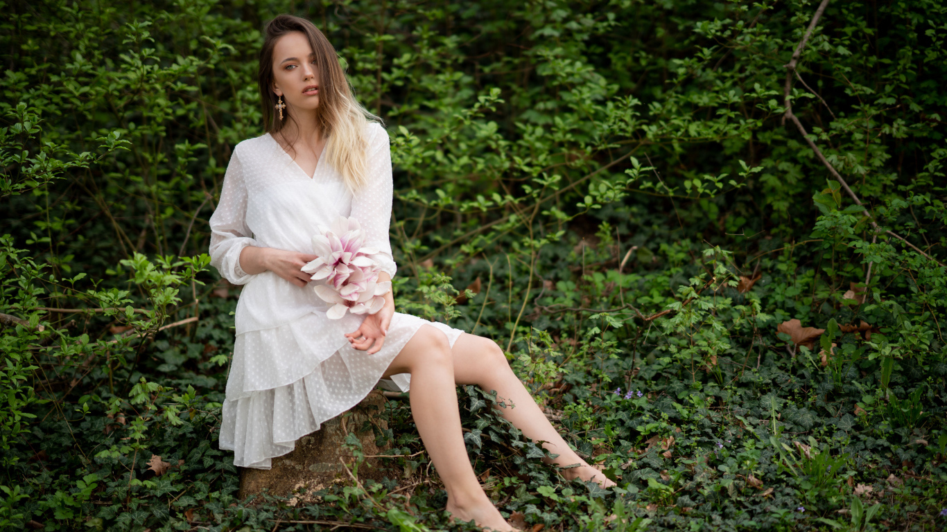 Молодая девушка в белом платье сидит на камне в лесу 