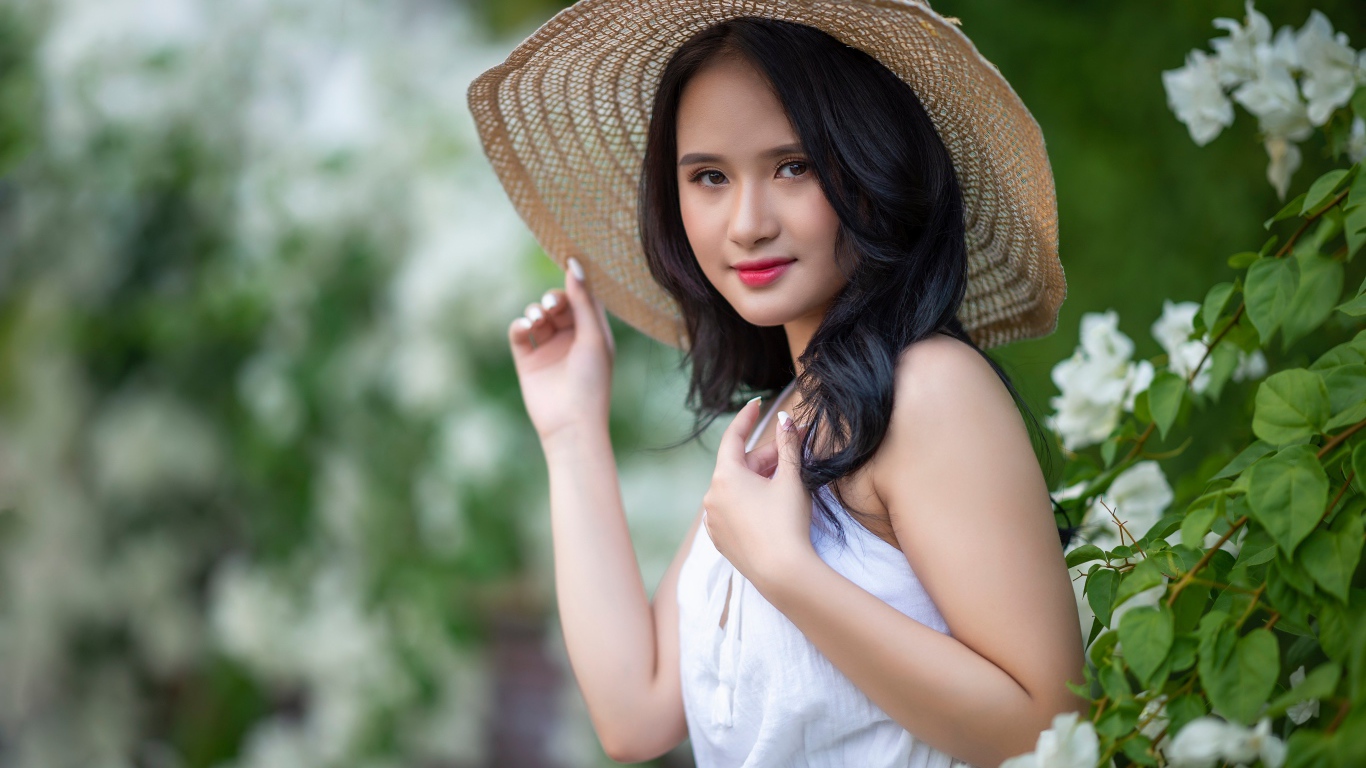Девушка азиатка в большой шляпе у зеленого куста