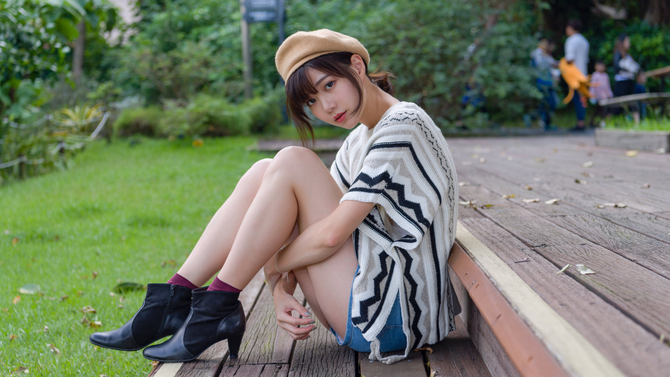 Девушка азиатка сидит в парке на лавке 