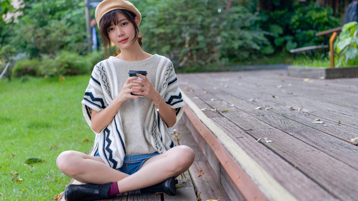 Девушка азиатка сидит с кофе в осеннем парке 