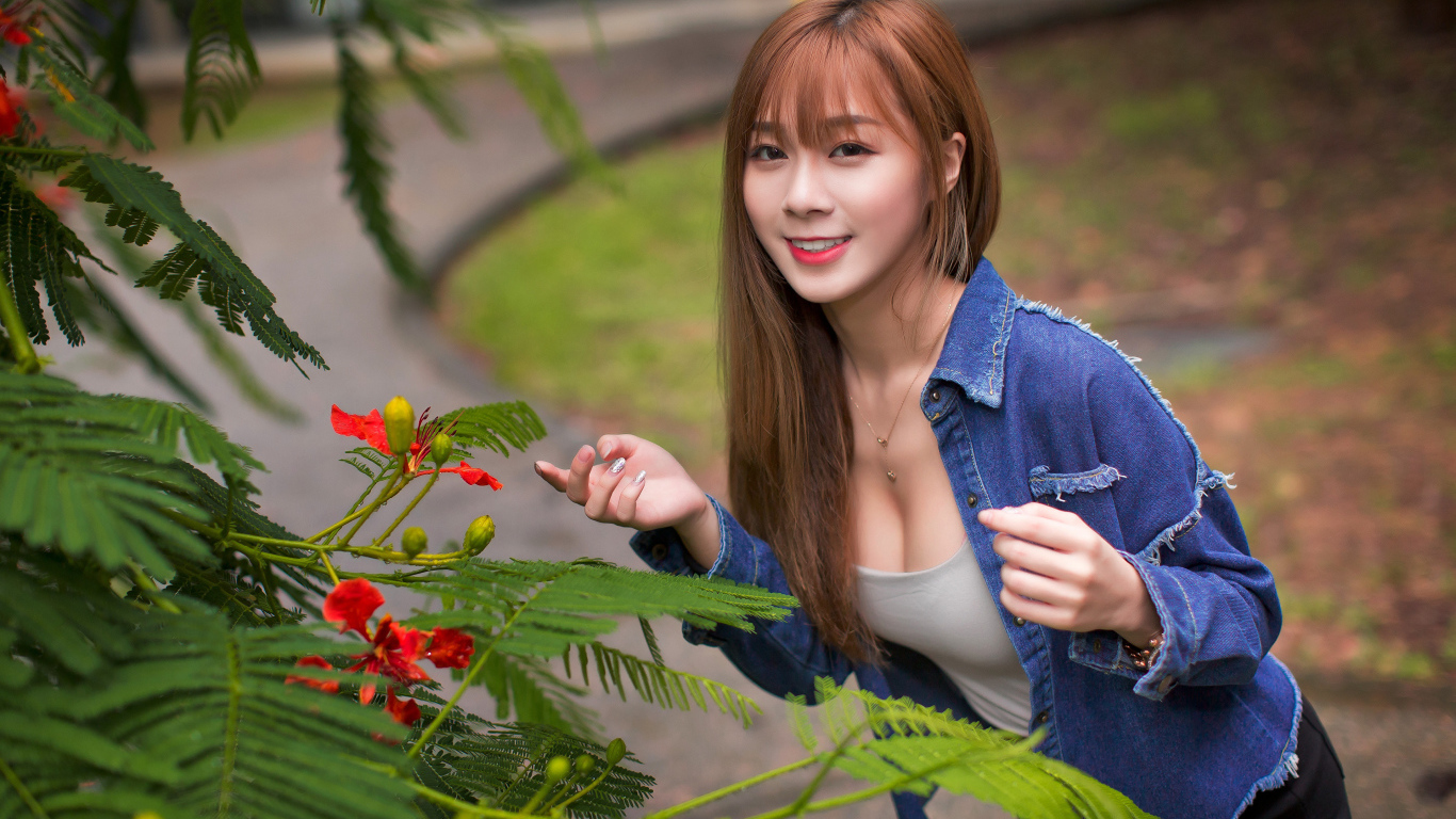 Девушка азиатка стоит у растения с зелеными листьями