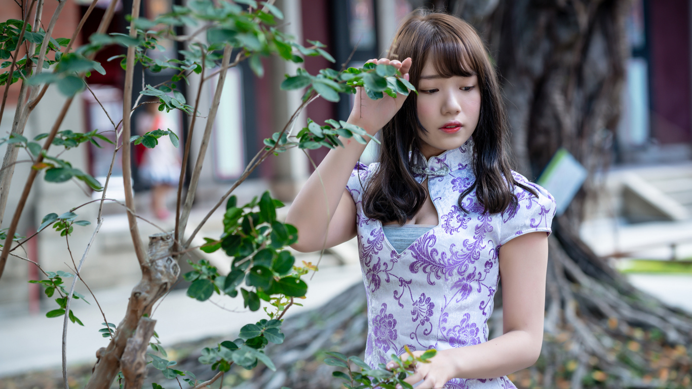 Красивая девушка азиатка в платье стоит у дерева 