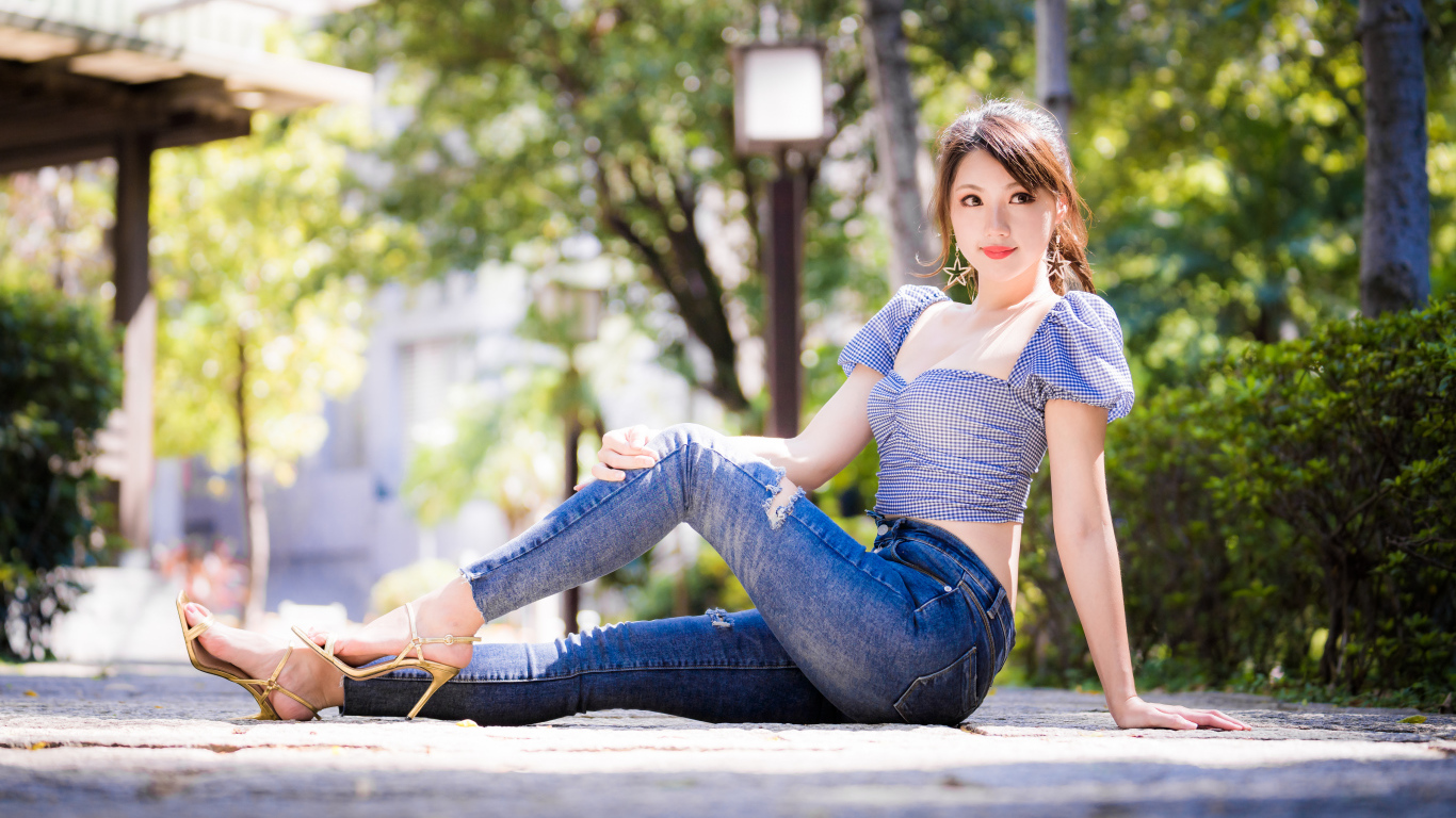 Красивая азиатка в джинсах сидит на земле