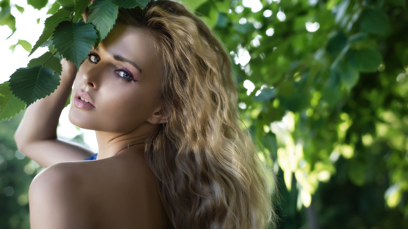 Красивая голубоглазая блондинка у ветки с зелеными листьями