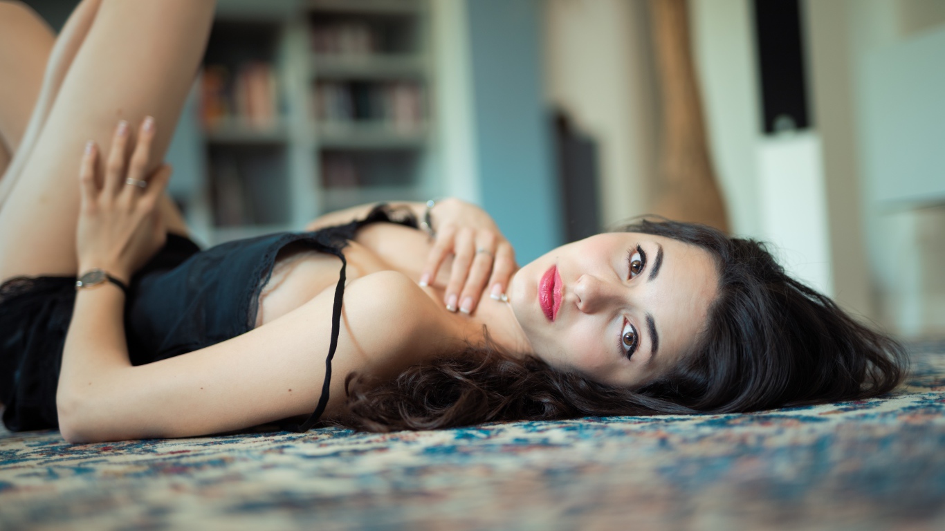 Красивая брюнетка в черном платье лежит на полу