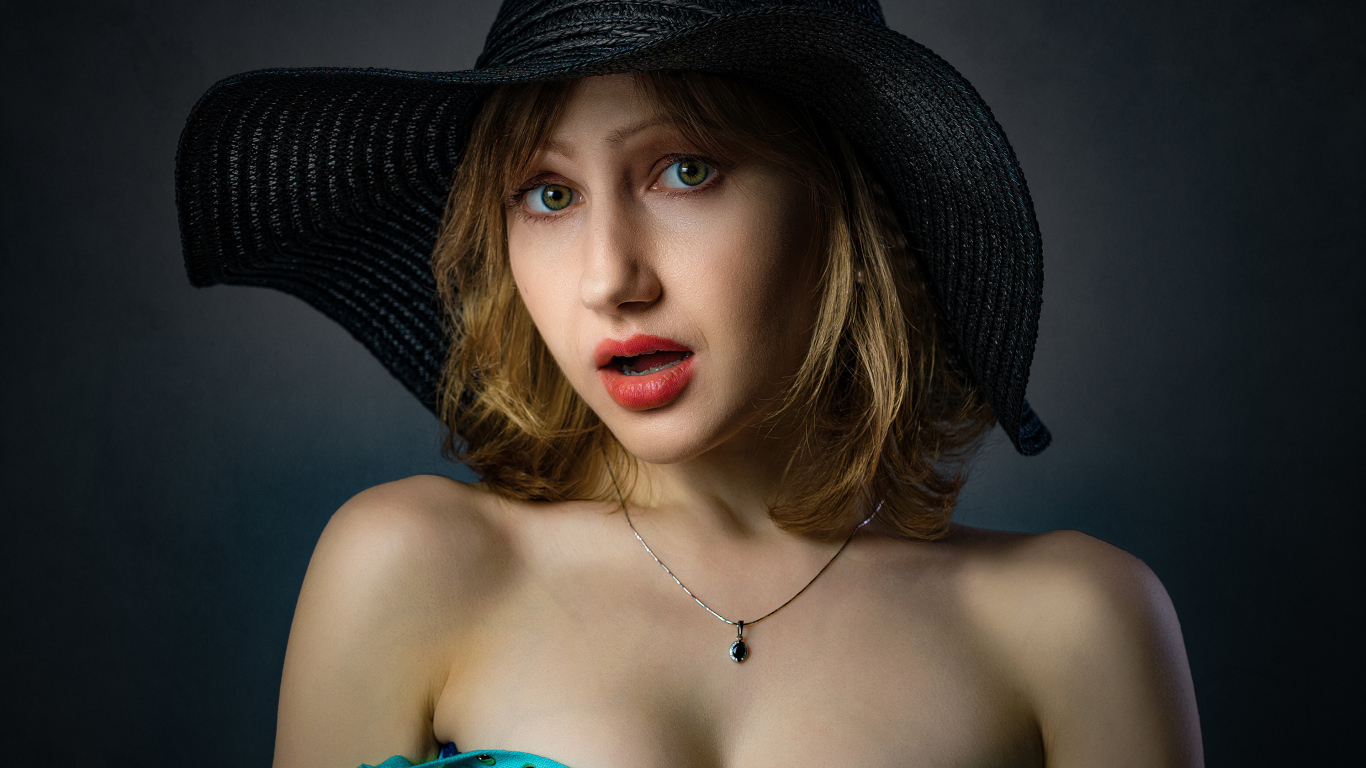 Красивая девушка в большой черной шляпе на сером фоне 