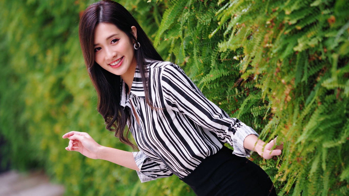 Красивая девушка в полосатой рубашке стоит у растения