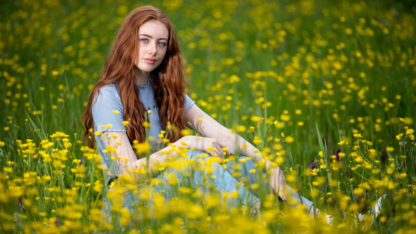 Голубоглазая девушка сидит на поле с желтыми цветами