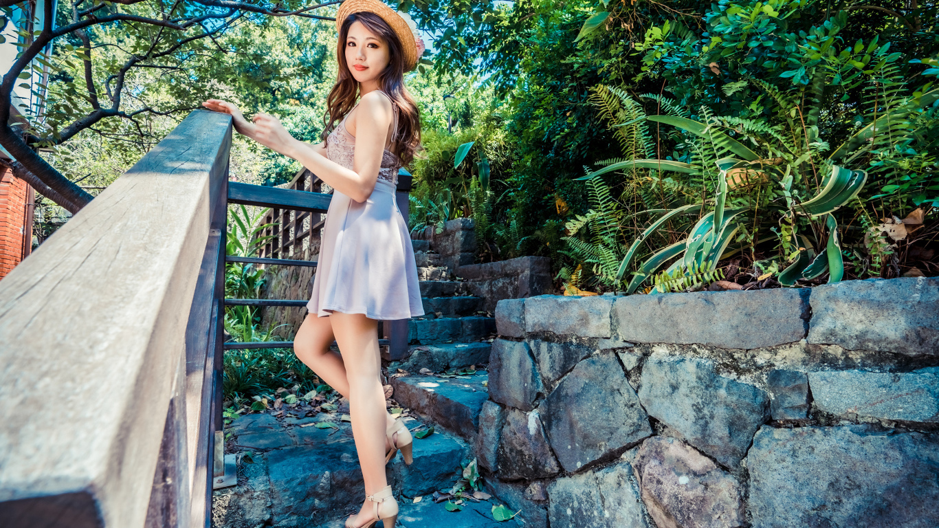 Милая девушка азиатка в платье стоит на ступеньках 