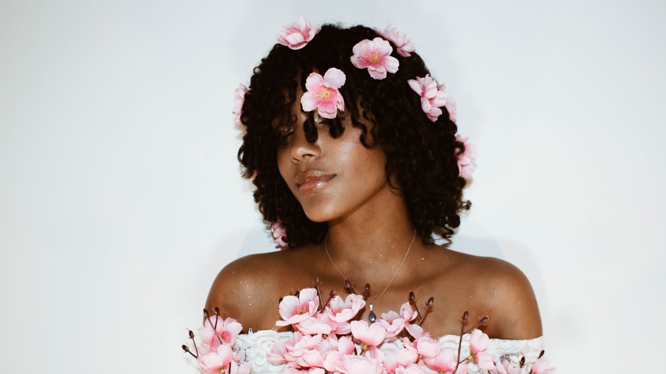Темнокожая девушка в розовых цветах на сером фоне